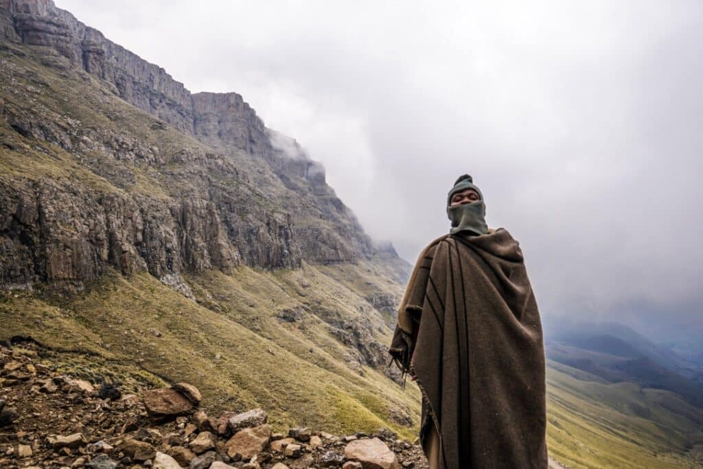 Traveler in traditional attire overlooking mountainous landscape in Lesotho.