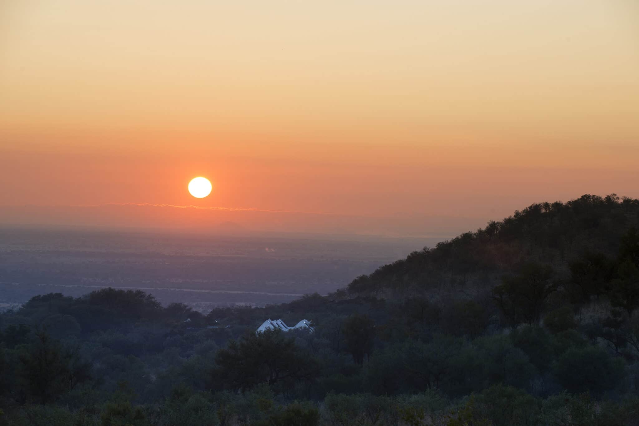 Beautiful sunset view over Pilanesberg with vibrant sky and silhouette of trees.