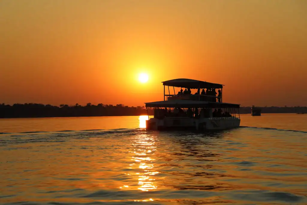 Sunset over Victoria Falls with boat on the Zambezi River.