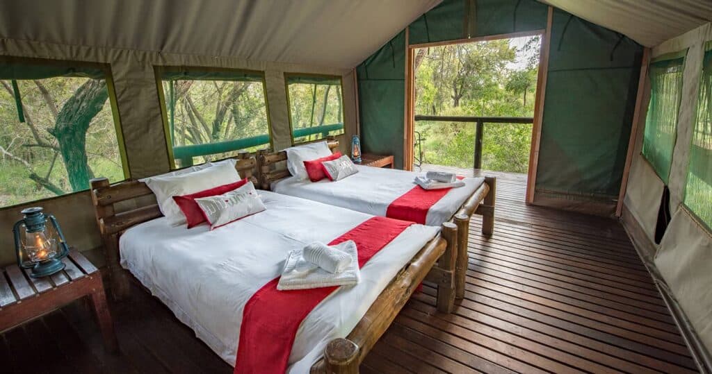 Luxurious tented camp room with three beds and scenic view of nature.