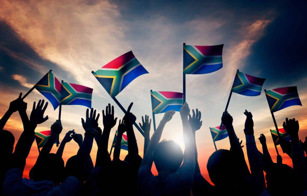 People waving South African flags during sunset celebration.