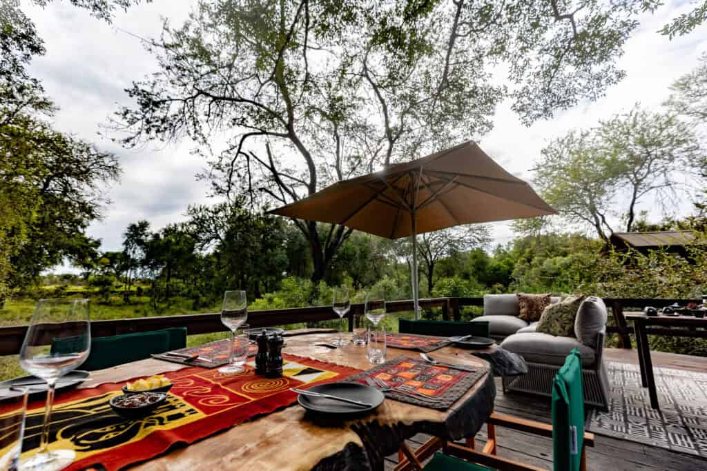 Outdoor dining setup at Ndzhaka Tented Camp with table, chairs, and umbrella.